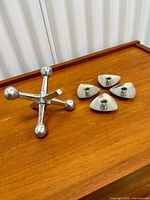 Group view of metal jack sculpture and four triangular candle cups on wood surface