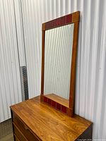 Full view of teak framed mirror with red tile accents on dresser