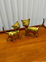 Both brass cat sculptures side by side on wood surface
