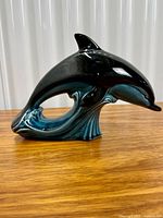 Left side profile of teal and black ceramic dolphin figurine on wood surface
