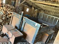 Left side view of the dump trailer showing bed, hydraulic cylinder, pump box, wheels and surrounding barn interior