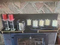 All items on mantel: pair of glass candlesticks with red candles, black metal hurricane with LED candle, five-candle centrepiece with cream candles