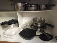 Shelf with stainless pots and pans, enamel roaster, Corning Ware casserole, griddle visible