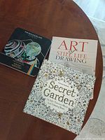 Lot overview showing Prismacolor pencil tin, Secret Garden colouring book, Art Of Still Life Drawing book