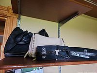 Black hobo bag, beige studded bag and black cinch belt on shelf