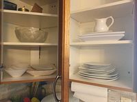 Open cupboard showing glass bowl, white bowls, platters, plates, pitcher