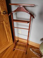 Full view of wood valet stand showing hanger, tray, trouser bar, casters