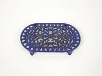 Top view of blue enameled cast iron oval trivet showing scrollwork pattern and rust spots