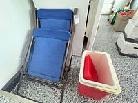 Two folded blue fabric metal chairs beside red cooler