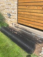 Side view of large and smaller rolls of black plastic fencing against house wall