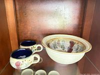 Front view of bowl and two mugs displayed on shelf