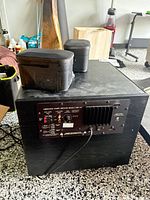 Rear view of subwoofer showing model PAM 1.2L amplifier panel and two speakers placed on top