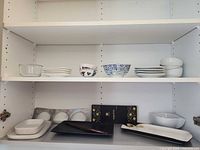 Cabinet shelves showing assorted sushi dishes, bowls, plates, chopsticks