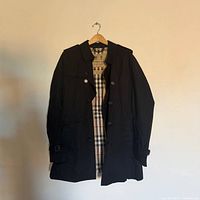 Full view of black Burberry Kensington trench coat on hanger showing exterior and lining