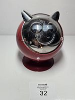 Front view of red spherical metal ashtray with silver cat face lid