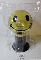 Front view of sealed yellow smiley face gumball dispenser on black base