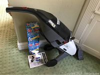 Photo of the Oreck Rinse-A-Matic steamer unit positioned on a green carpet with two pet carpet care kits, a stain spray bottle, and user manual placed nearby.