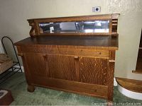 Front view of the antique wooden sideboard showing three keyed drawers, mirror along back, wooden cabinet doors, and overall chunky design.
