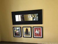 Rectangular faux woven wall mirror with black frame hung above three framed vintage advertisement prints.
