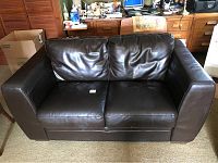 Front view of black leather loveseat with two seat cushions and two back cushions, showing some creases and wear marks.