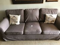 Front view of the brown Ikea Ektorp sofa showing three seat cushions, two back cushions, and two decorative bird pattern pillows at the sides.