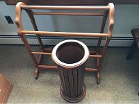 Photo showing top view of wooden blanket rack and wooden umbrella stand on floor, blanket rack has three horizontal bars, umbrella stand is cylindrical with vertical slats.