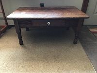 Front view of a natural wood farmhouse coffee table showing the drawer with porcelain knob and turned legs.
