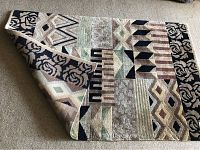 Indian wool rug folded showing striped Transatlantic design in terracotta colors mixed with beige, black, greens, and browns.