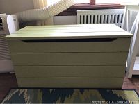 Front view of light green painted wooden chest showing horizontal slats and cut-out handles on sides.