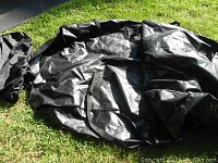 Black soft rooftop cargo carrier laid flat showing size and texture on grass with storage bag beside it.