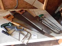 Photo showing assortment of hand saws and hand files on wooden surface