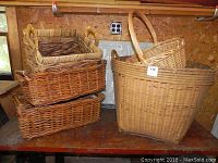 Photo showing 4 wicker baskets stacked and nested with natural light beige to brown hues on wooden surface with wood panel background.