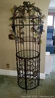 Full view of the bronzed metal wine bar showing scrollwork, decorative flower and grape vine embellishments, round glass top, and artificial leaf and grape decorations.