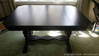 Front view of black painted wooden dining table showing top surface and carved legs