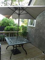 Full view of square patio table with umbrella inserted, placed on wooden deck.