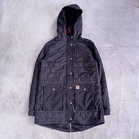 Front view of hooded quilted jacket showing color, pockets, logo patch, drop-tail hem