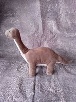 Full left side view of brown and white brontosaurus plush standing