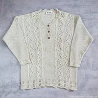 Full view of cream cable knit sweater laid flat