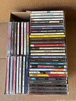 Box with approximately 28 music CDs in jewel cases stacked in two rows