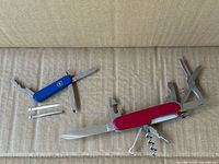 Both Swiss Army knives open displaying tools and loose tweezers
