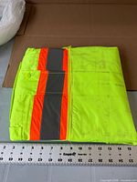 Folded used safety jacket showing reflective stripes and dirt marks with ruler for scale