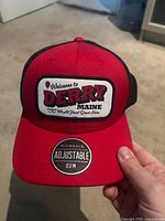 Front view of red and black Bioworld trucker hat with Welcome to Derry patch and Bioworld adjustable sticker