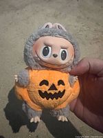 Front view showing Labubu face in grey hood and orange pumpkin body