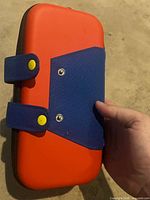 Front view showing orange panel, blue strap, snap buttons, black zipper