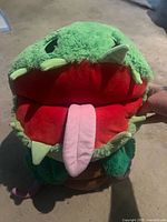 Front view showing green plant head, red mouth, pink tongue, felt teeth, parts of brown pot