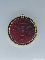 Front view showing carved red disc, black cabochon border and gold-tone bail loop