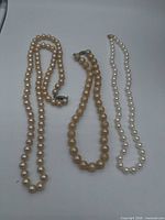 Three pearl necklaces laid out showing color differences and clasps