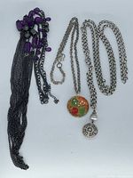 Three necklaces laid out: Chico's purple multi-strand, Brighton pendant, Silpada lariat