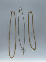Three necklaces laid flat: two rope chains and one fine chain with bail