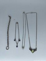 All four jewellery pieces laid out: chunky bracelet, flower-charm necklace, X-pendant necklace, heart-pendant necklace